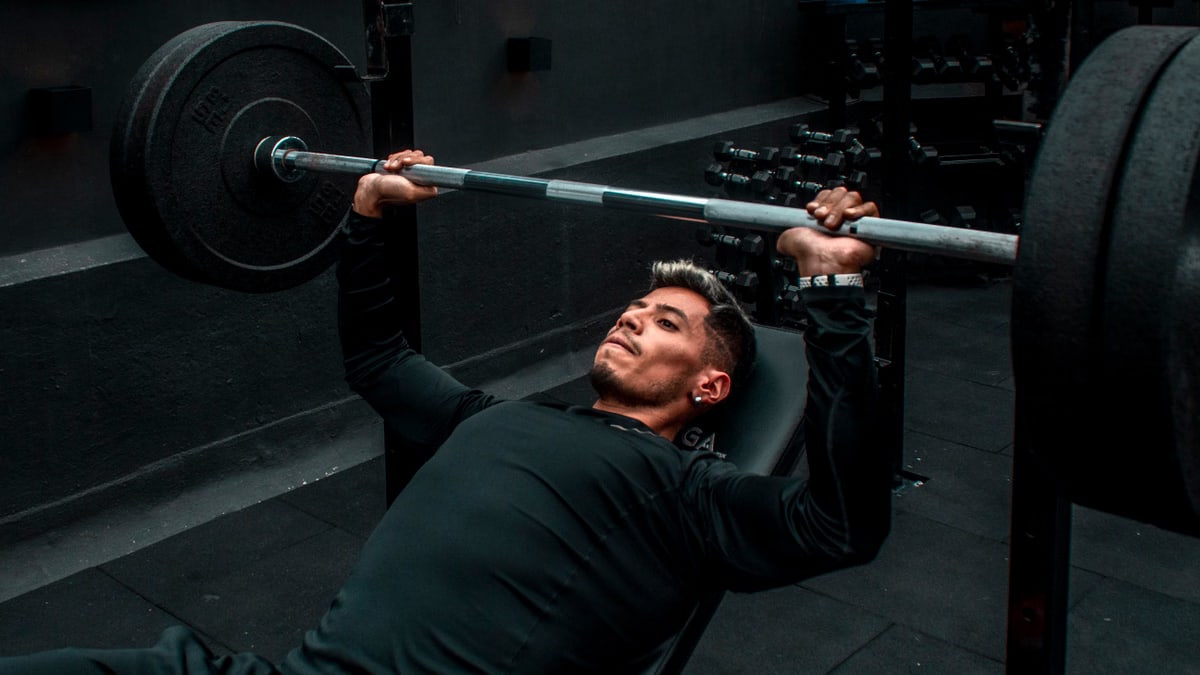 Man performing bench press with heavy barbell in a gym setting, focusing on strength training.